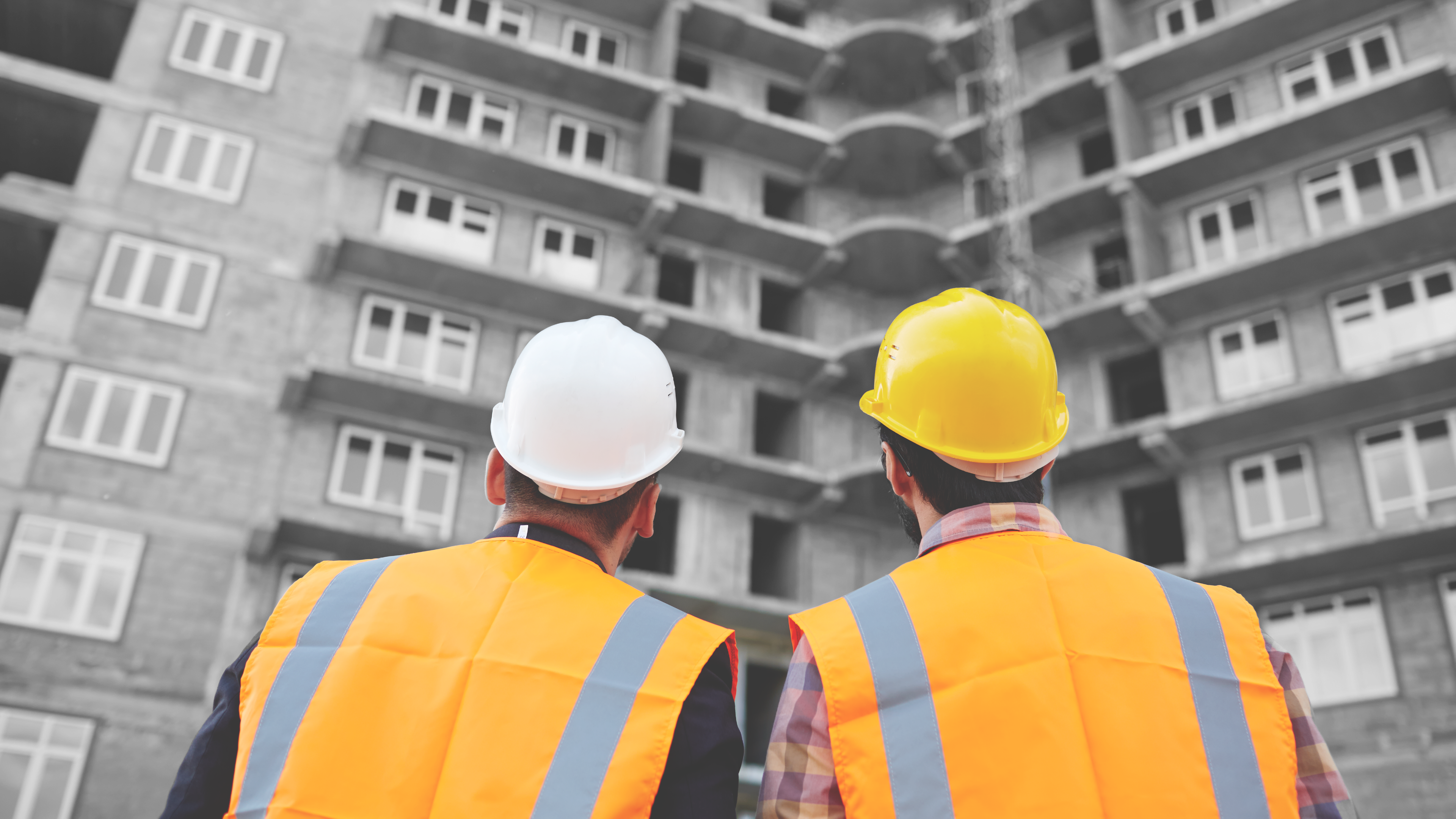 Imagen de dos hombres en uniforme de constructor observando un edificio de apartamentos